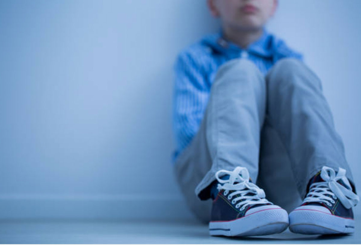 Boy with social anxiety sitting by himself against a wall.
